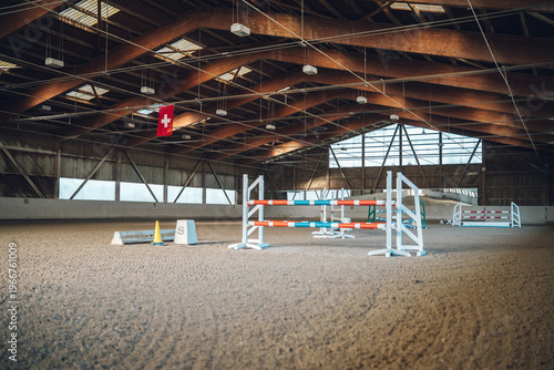 Tableau sur toile Empty indoor arena setup for show jumping with colorful obstacles and a swiss fl