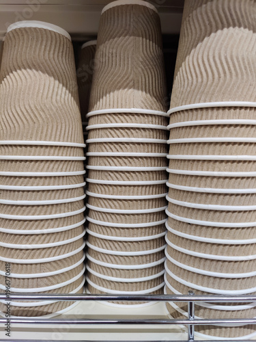 Stacks of beige disposable biodegradable cardboard cups for hot cold drinks on shelf in store. Close-up.