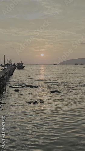 Video of a sunset view at the pier, there is a boat docked with the sunset and island in the background.