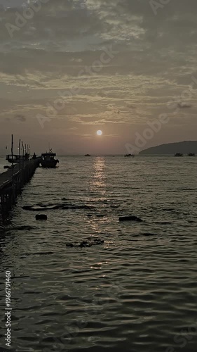 Video of a sunset view at the pier, there is a boat docked with the sunset and island in the background.
