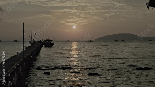 Video of a sunset view at the pier, there is a boat docked with the sunset and island in the background.