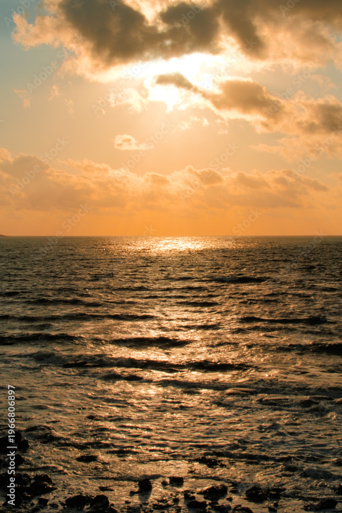 Fototapeta premium Dramatic orange sunset clouds over dark ocean waves with sun rays
