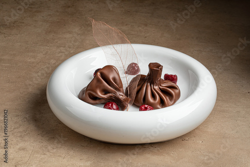 Creative chocolate dessert shaped like khinkali with berries and decoration served on white plate