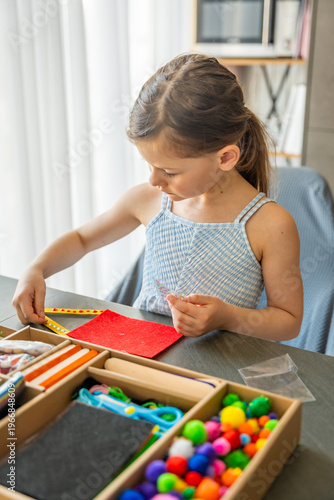 Little girl decorating handmade craft with colorful self adhesive rhinestones at table. Kids creativity fine motor skills development and learning through play concept.