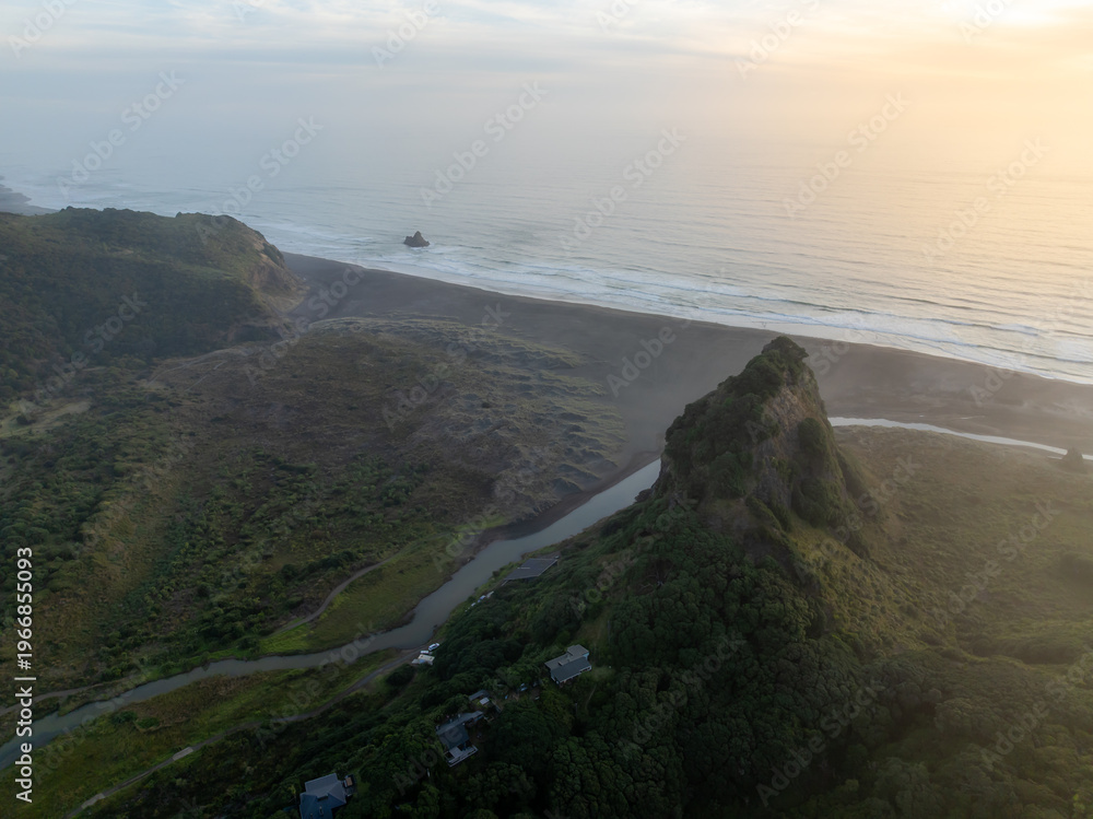 Naklejka premium Aerial view of the black sands of Karekare Beach, New Zealand, with the iconic Lion Rock and lush green hills. A popular destination for surfers and nature lovers.
