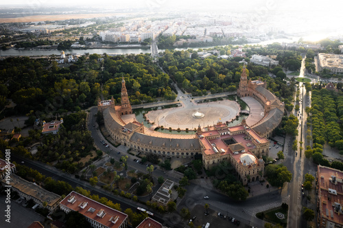 Aerial view of the semicircular Plaza de Espana with its grand towers and canal surrounded by lush greenery in Seville, Andalusia, Spain.
