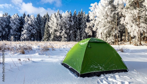 Green tent pitched in a serene winter landscape with snow covered trees.