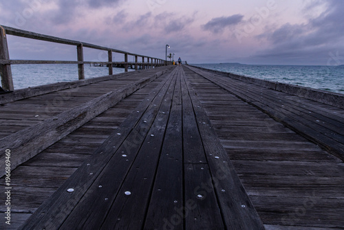 pre-dawn on an old timber jetty with someone going fishing in the distance