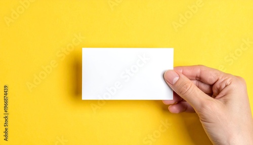 Hand holding a blank white card on a vibrant yellow background.