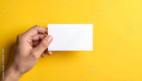 Hand holding a blank white card against a vibrant yellow background.