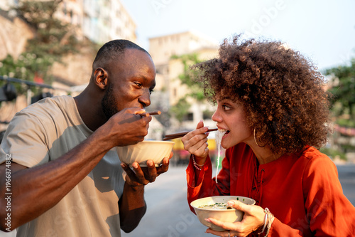 Happy black couple traveling and enjoying exotic street food with chopsticks, having fun