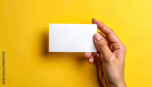 Hand holding blank white business card on vibrant yellow background for branding.