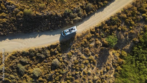 Aerial view of a white camper van traveling along a winding dirt road through the rugged, golden landscape of Limnos Island, Greece, highlighting the freedom of off-grid exploration.