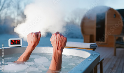 Two clenched fists rise from a frigid ice bath as steam billows into the freezing air. Outside winter sauna for intense recovery session. Discipline, and extreme physical challenge therapy concept