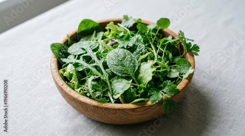 A wooden bowl filled with mixed leafy greens sits on a table indoors.