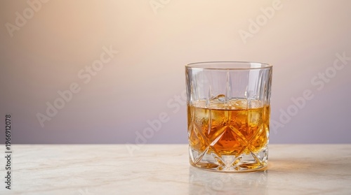 A glass of whiskey sits on a table with ice cubes inside.