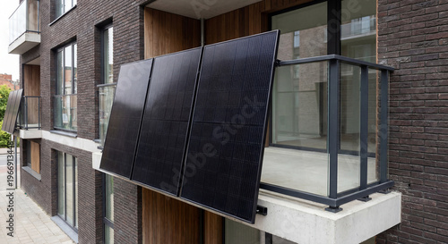 A side view of a row of three black solar panels mounted at a slight angle on the balcony of a modern apartment