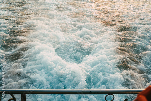 Ship stern cutting through cold waves at golden sunset. Dynamic seascape, travel adventure and maritime lifestyle concept.