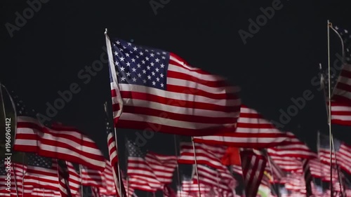 Field of USA flags at night in Malibu, California, USA with silhouette figure in foreground illuminated by strong lights, emotional patriotic tribute scene