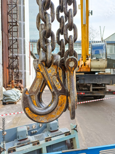 Close up of massive steel crane hooks on chains with truck crane on background