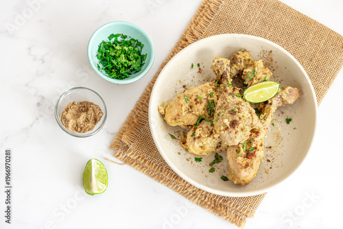 Creamy Spiced Chicken Drumsticks with Lime and Fresh Herbs on Marble Background, Top View