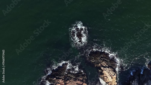 Waves move in and out among rocks at a coastal area during the day. The water splashes and creates foam as it hits the hard surfaces, showing the power of the ocean.