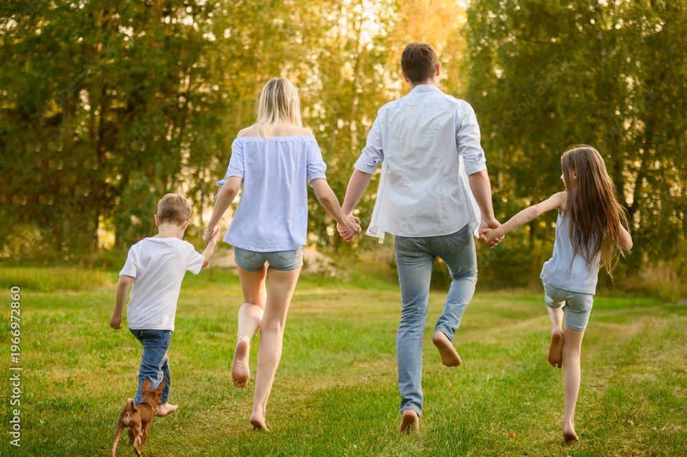 Obraz premium Happy Family Running Barefoot on Green Grass in Summer Park, Back View of Parents and Children Holding Hands. Freedom and Togetherness Concept, Rural Vacation, Leisure Time, summer holidays
