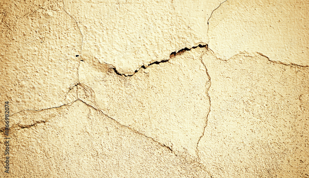 Obraz premium Dilapidated stone wall with deep cracks and peeling stucco. Warm sepia tones and vignette filter processing