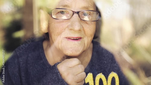 Portrait of an elderly woman with glasses holding anniversary candles.  An old woman holds a birthday cake alone on her centenary.