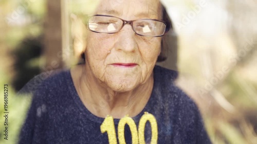 Portrait of an elderly woman with glasses holding anniversary candles.  An old woman holds a birthday cake alone on her centenary.