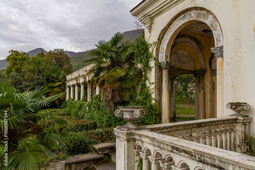 Abandoned railway station with classical columns and arches overgrown with tropical plants and ivy. Ruined vintage architecture in spring. Gagra, Abkhazia, Caucasus.