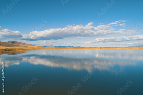 Aerial view of the clouds reflect on still water at the lake during the day in a natural landscape with mountains in the background