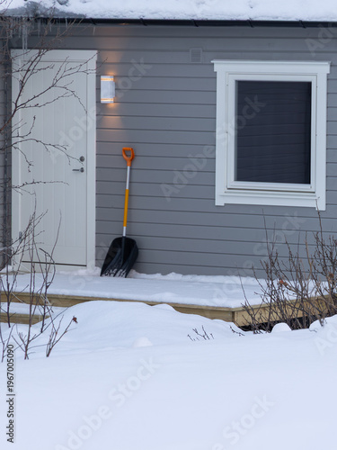 Snow shovel on the porch next to the door, ready for winter