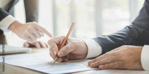 Signing a business contract with one hand signing the document while the other person points a finger demonstrates a business agreement.