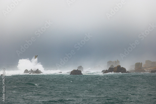 View of powerful waves crashing against jagged rocks in a misty and stormy sea Ushant, Brittany, France.