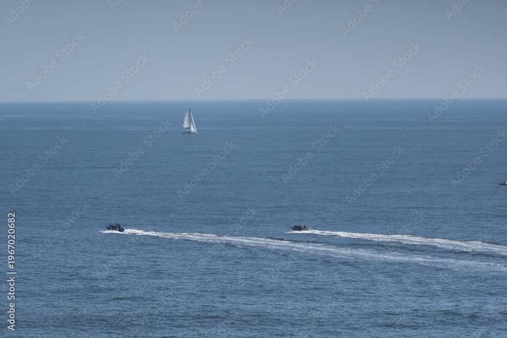 Obraz premium A serene seascape with small boats floating on clear blue water under a partly cloudy sky, capturing a peaceful maritime scene.