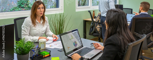 Two female colleagues in a coworking setting engaging in conversation, one expressing surprise while discussing a topic with her coworker during work hours. Businesswomen talking about rumor in office
