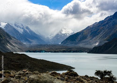 View of glacier covered with moran across a glacial lake with clouds and snow capped mountains