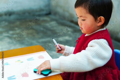 Focused Asian toddler girl learning to clean and organize at a small desk. Adorable child developing fine motor skills and good habits at home.