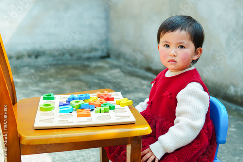 Cute Asian toddler girl playing with colorful alphabet puzzle at a small desk. Little child learning letters and early education at home or daycare.