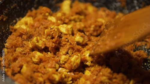 Close-up of cooking pilaf ingredients with chicken and carrots in a frying pan. Wooden spatula stirring sizzling food. Authentic homemade meal preparation, traditional cuisine, healthy and delicious.