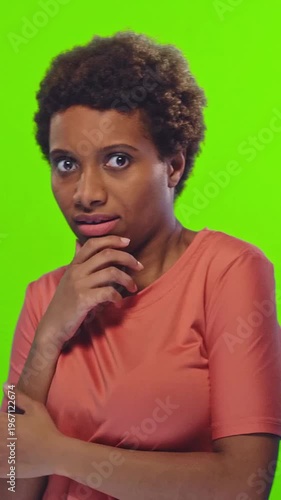 Young African American woman with short curly hair in orange t shirt expressing surprise and fear with wide eyes and open mouth on green background in studio. Emotion, reaction and shock.