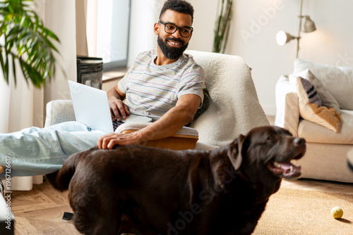 Photos Happy man working remotely from home, petting his dog in a bright living room