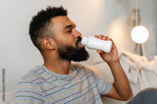 Quadro su tela Young black man with a beard drinking a healthy probiotic beverage from a bottle