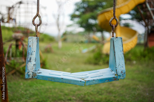 Broken plastic children's swing on the playground, old and unsafe swing. Old blue swing in an abandoned outdoor playground rustic environment