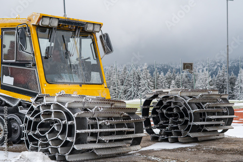 Fotografi Close-up of snow groomer tracks, yellow snowcat machine covered in frost, heavy winter equipment at ski resort, slope maintenance machinery, winter technology in the mountains