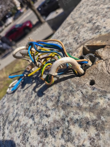 Exposed electrical wires protruding from granite surface on city sidewalk with tangled colored cables showing damaged infrastructure