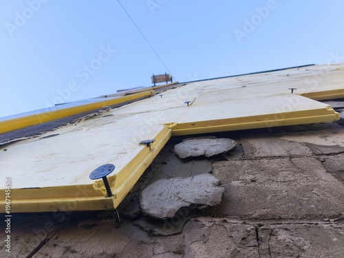 Low angle view of building facade under renovation with yellow insulation boards and exposed damaged concrete wall under blue sky background