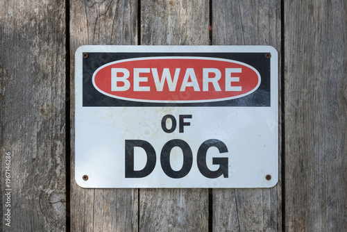 Image of beware of dog sign nailed to wooden backyard fence.