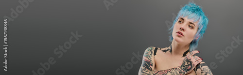 Tablou pe pânză Vibrant young woman with stylish blue hair and colorful tattoos expressing confi